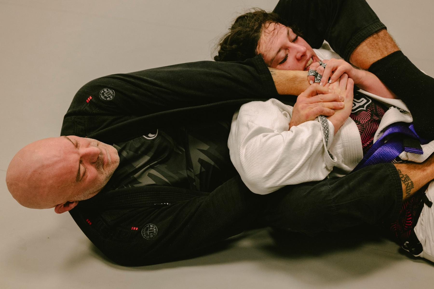 Black belt in a black gi applying an armlock on a purple belt in a white gi