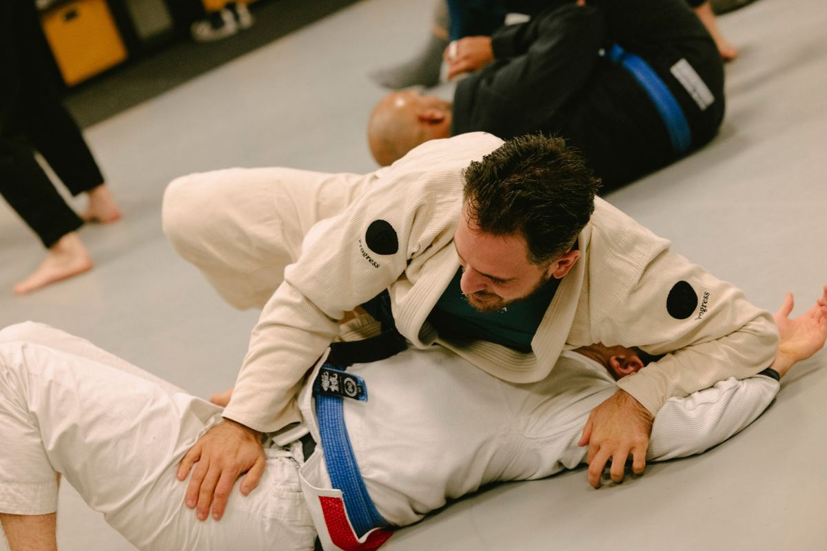Student in a cream gi holding side control on a blue belt