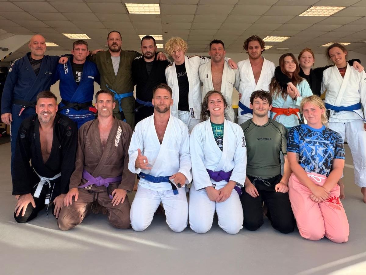 The Poole BJJ team in gis and rash guards, standing and kneeling together on the mats
